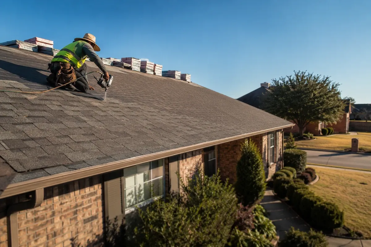 Roofing crew installing architectural asphalt shingles on a single-story Texas brick home under a clear summer sky